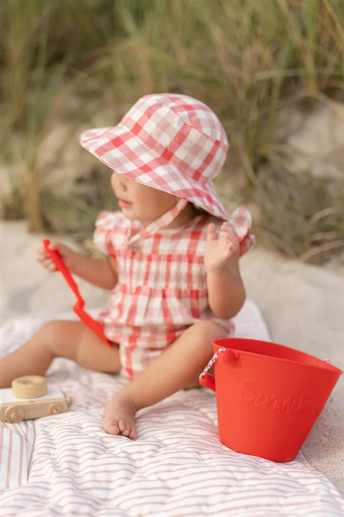 kind met srunch oprolbare silliconen emmer op het strand. Kleur koraal