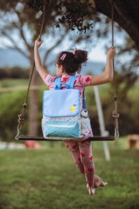 meisje op schommel met kleurrijke kinderrugzak voor uitjes en school